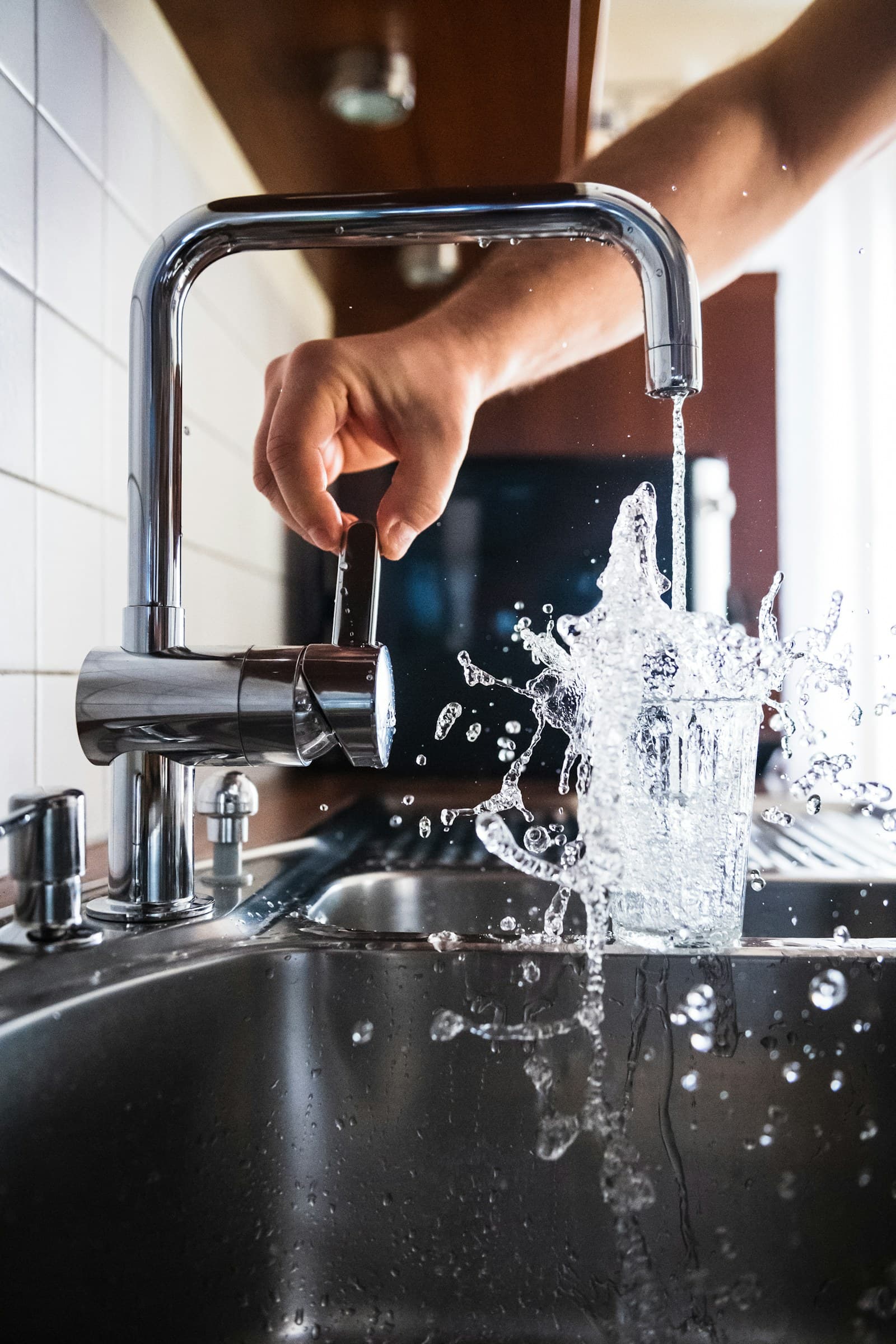 Kitchen tap running into a glass, water caught mid-splash